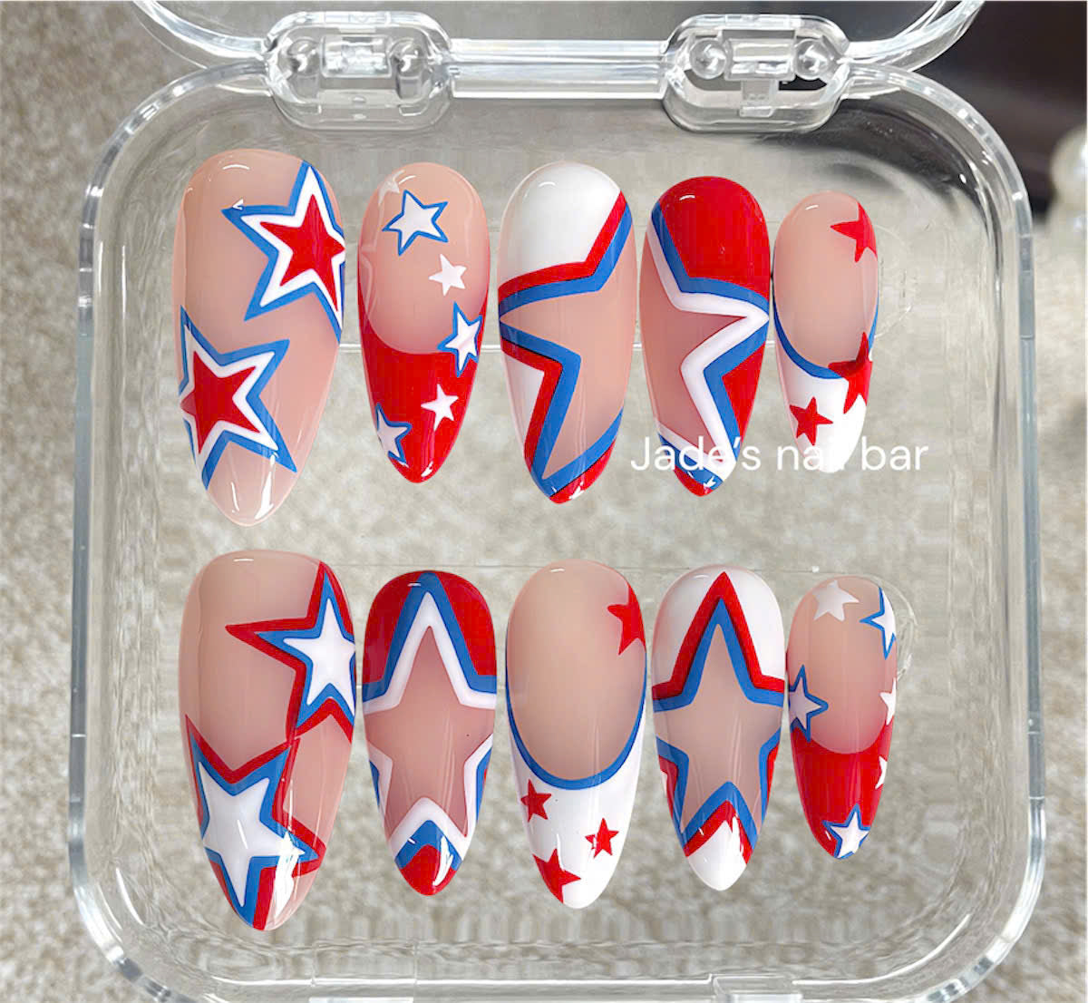 A set of 10 false press-on nails displayed in a clear plastic case, featuring a patriotic red, white, and blue star pattern on a nude base.